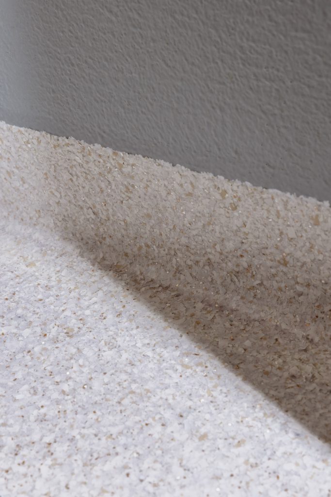 Detail of a light seamless flake coating with cove skirting up against a grey wall