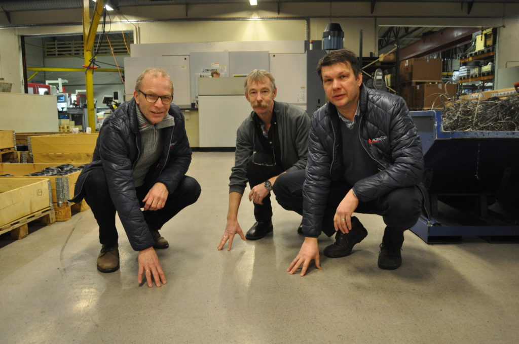 Three men crouching to inspect a light industrial floor in a factory hall – from AcryliCon Rogaland's project in Asia