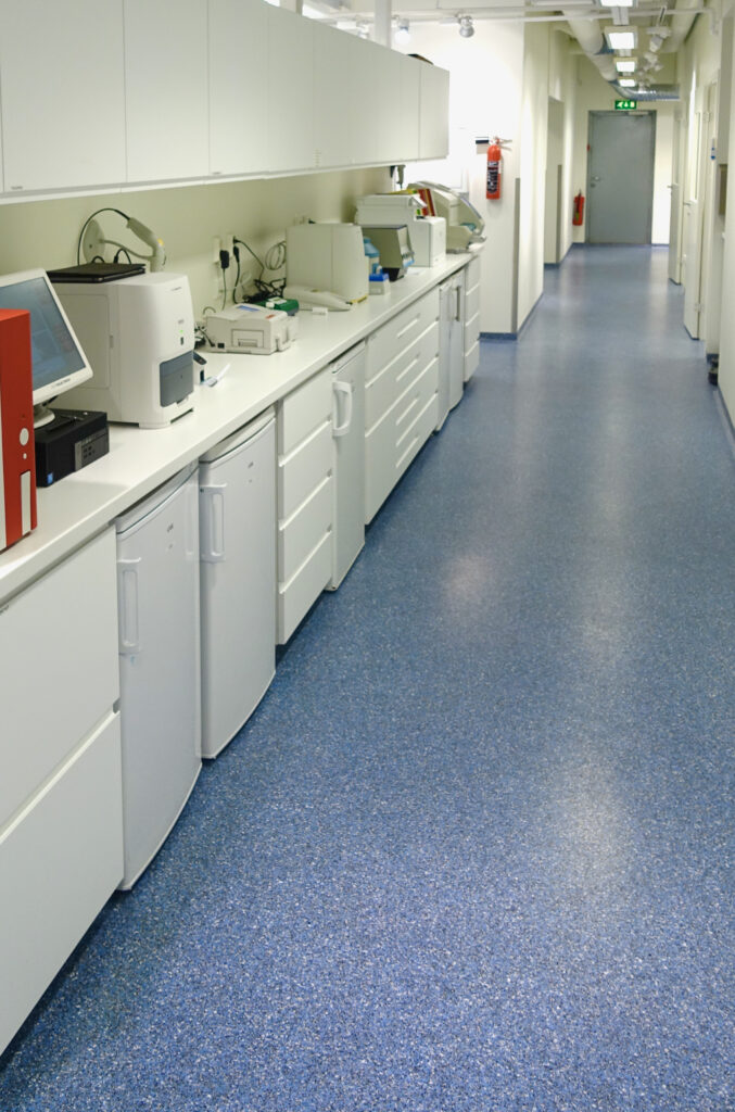 Blue seamless acrylic flooring in a long clinic corridor with white cabinets and laboratory equipment