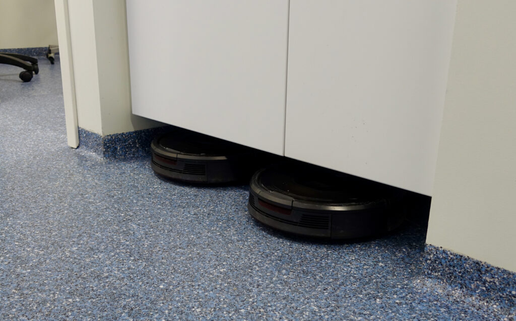 Two robot vacuum cleaners under cabinets on the clinic's blue seamless acrylic floor