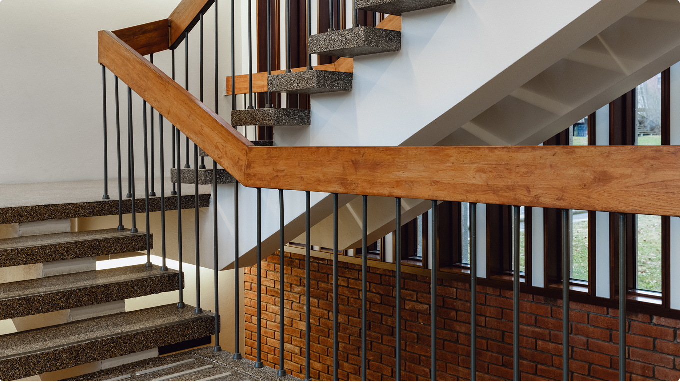 Stairwell with terrazzo steps, wooden handrail and brick wall